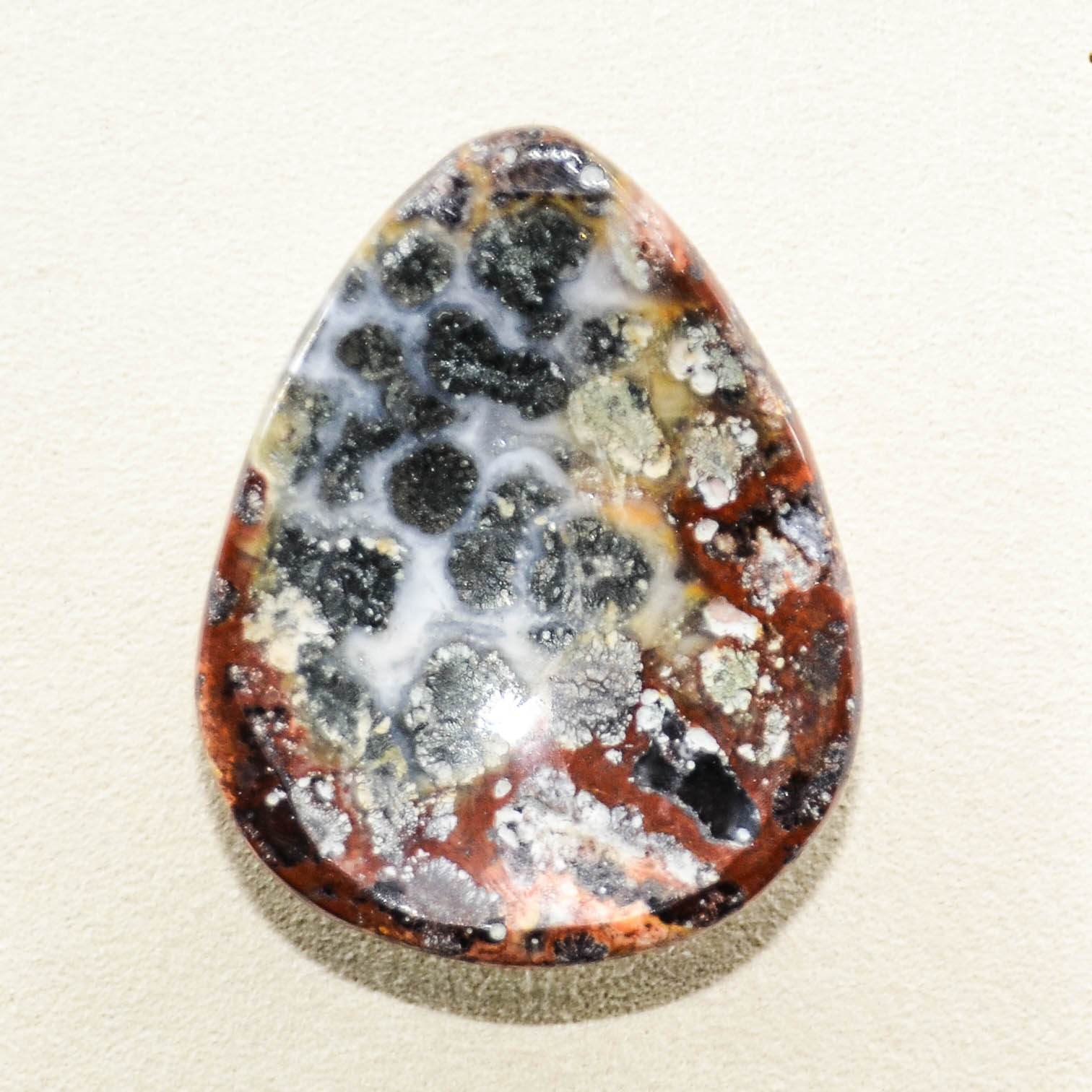 Polished Red Marcasite Worry Stone. Splashes of red, whites, and yellow. There are spots of grey throughout.